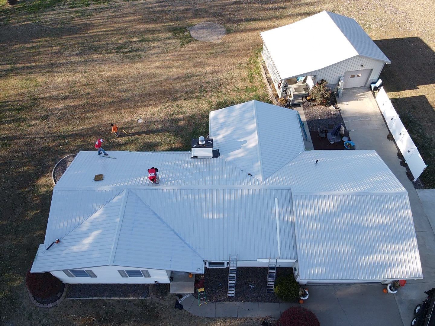 Aerial view of a large white-roofed house with an attached carport and a separate outbuilding.