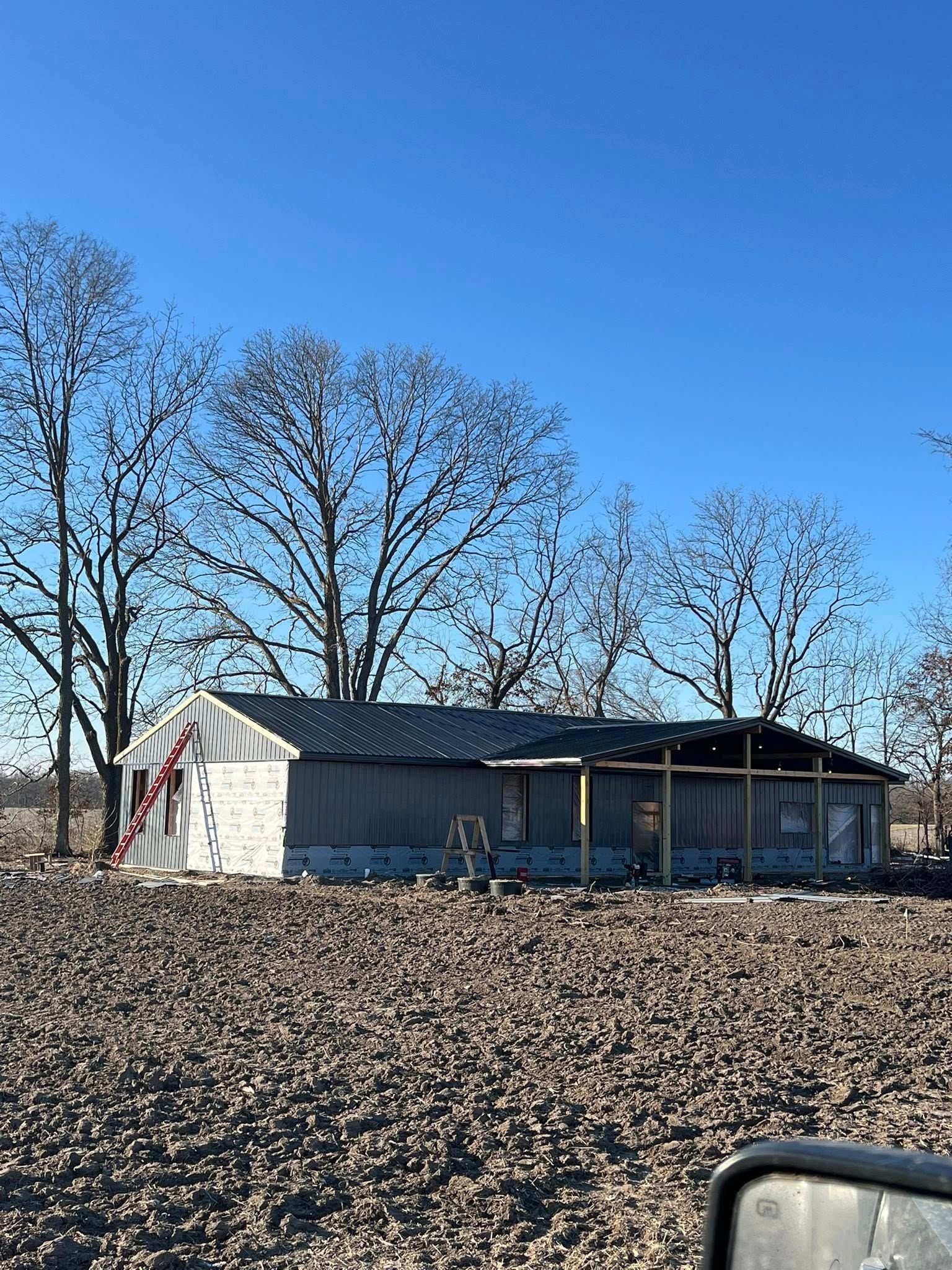 Small rural shed with a porch in a plowed field under a clear blue sky