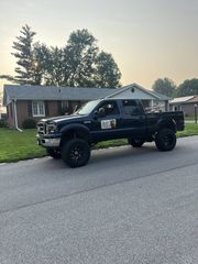 A lifted black Ford pickup truck parked on a residential street in front of a brick house at sunset.