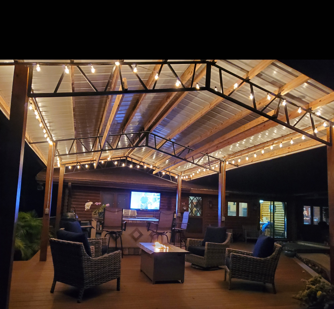 A patio with a gazebo, chairs and a table under a canopy at night.