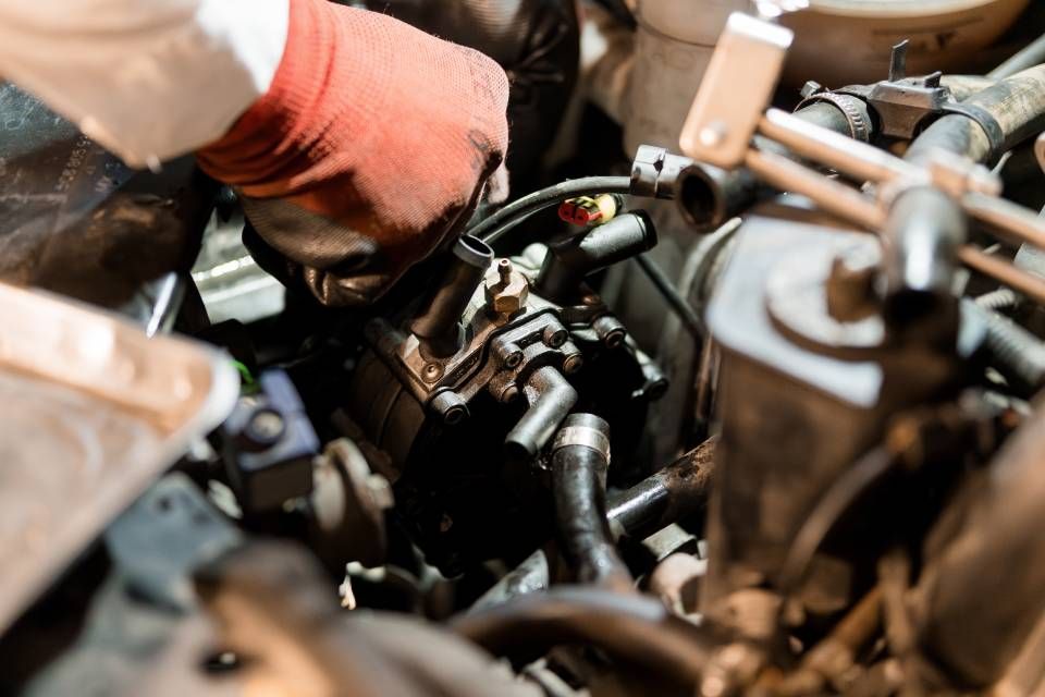 Mechanic in orange gloves working on a car engine with a wrench