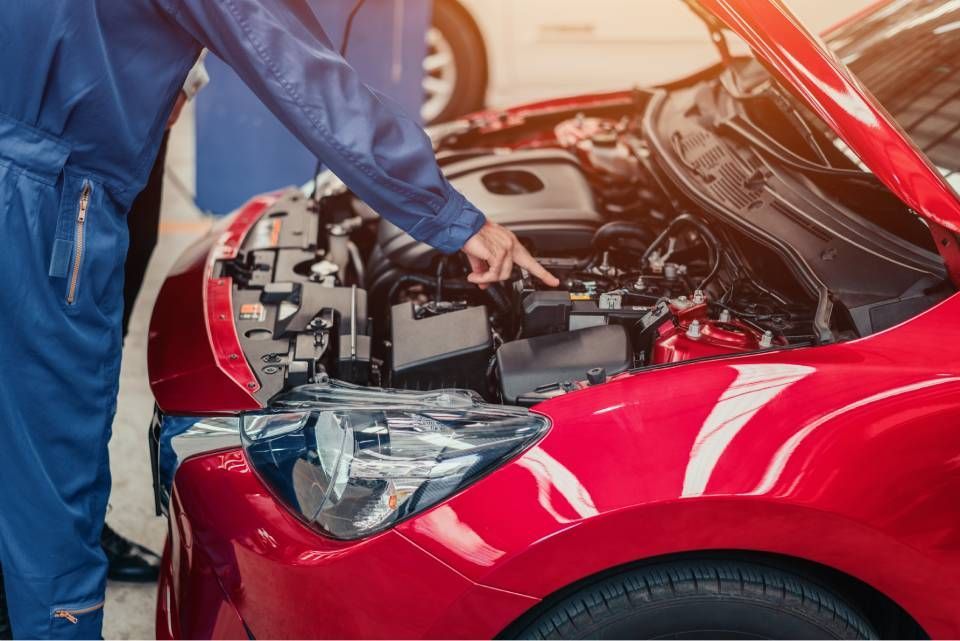 Mechanic inspecting a red car with its hood open in a repair shop