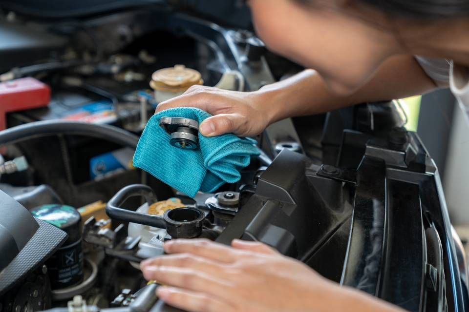 Person wiping a car engine with a blue cloth in a garage