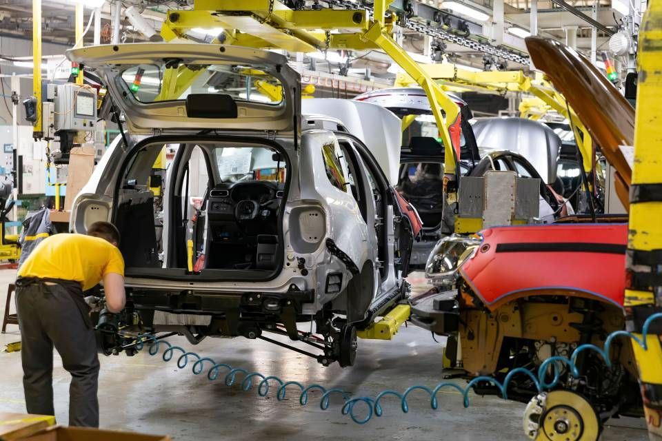 Car assembly line with workers installing parts on a silver vehicle chassis in a factory