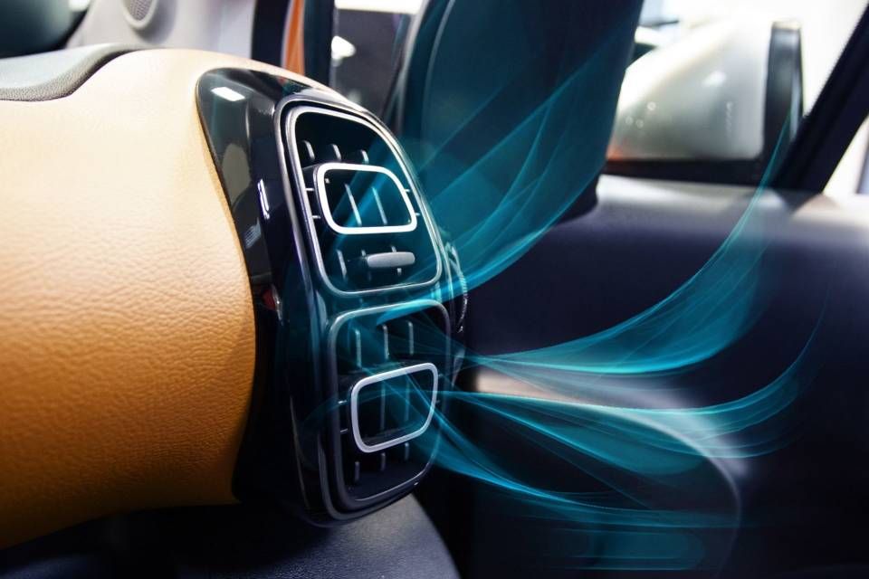 Close-up of a car air vent with blue airflow on a tan dashboard