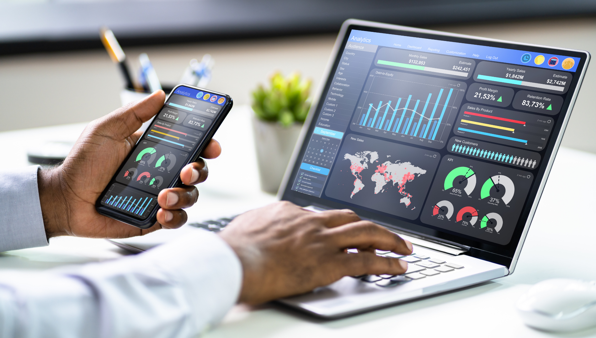 Person using laptop and smartphone, both displaying data visualizations, likely analytics dashboard.