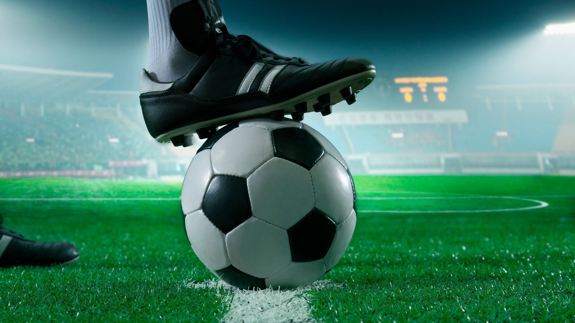 Soccer player's foot on a soccer ball on the field, illuminated by stadium lights.