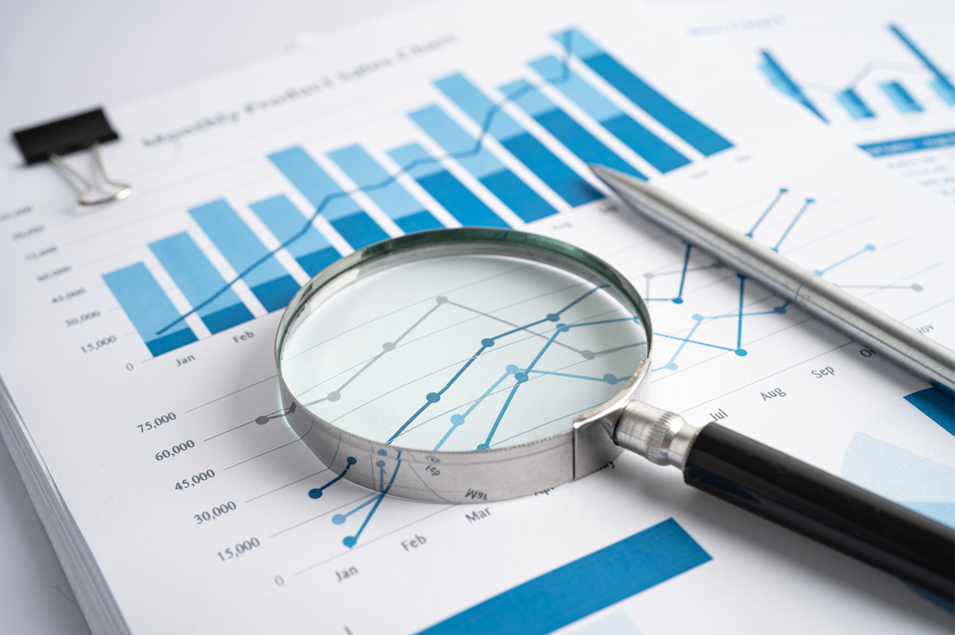 Magnifying glass on financial charts, analyzing sales data, with a pen.