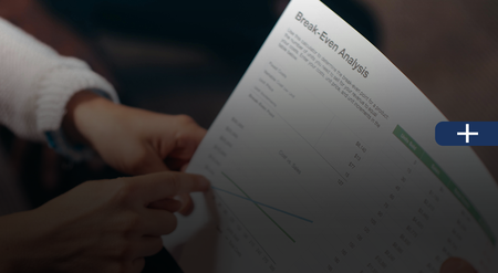 Hands pointing at a break-even analysis chart, discussing financial data.