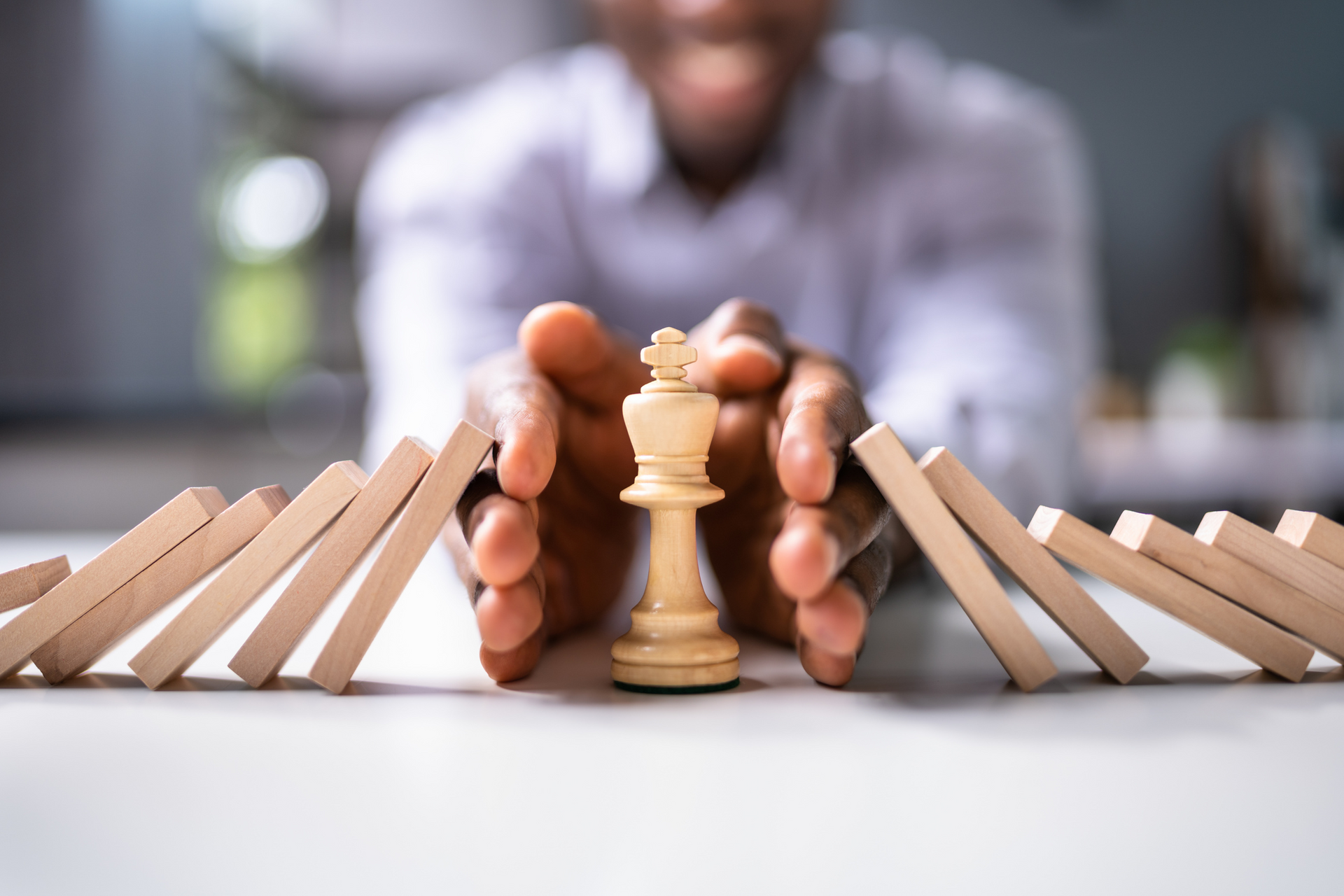 Person protecting a chess king from falling dominoes.