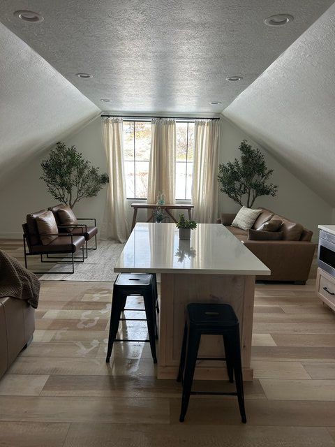 Bright attic-style living room with beige sofas, a long white table, stools, and tall windows