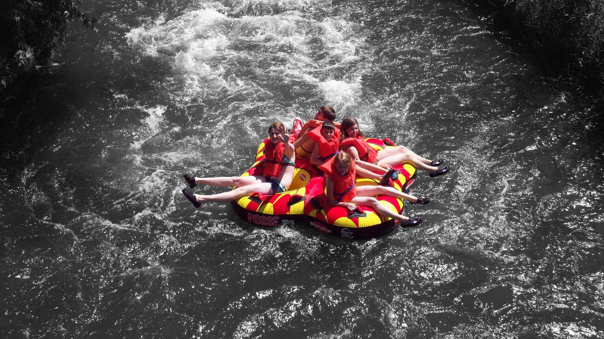 Group in bright life jackets floating in dark water on a rescue raft