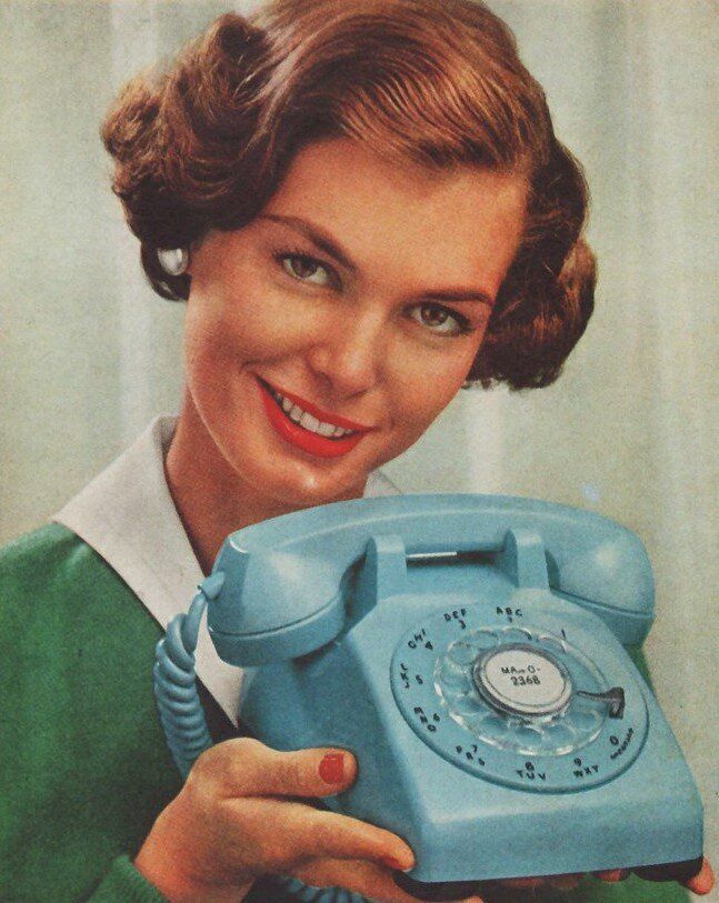 Smiling woman holding a light blue rotary telephone against a pale background