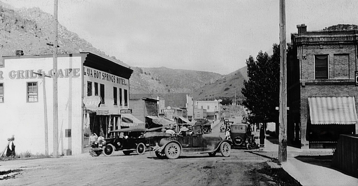 Vintage cars on a small-town main street with storefronts and mountains in the background