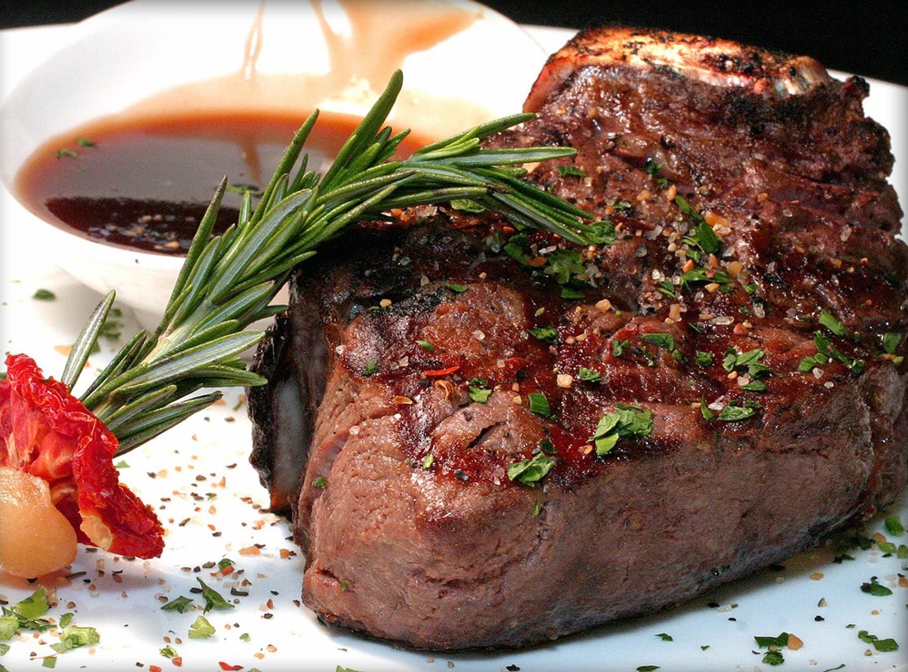 Grilled steak with rosemary and sauce on a white plate, garnished with herbs and tomato