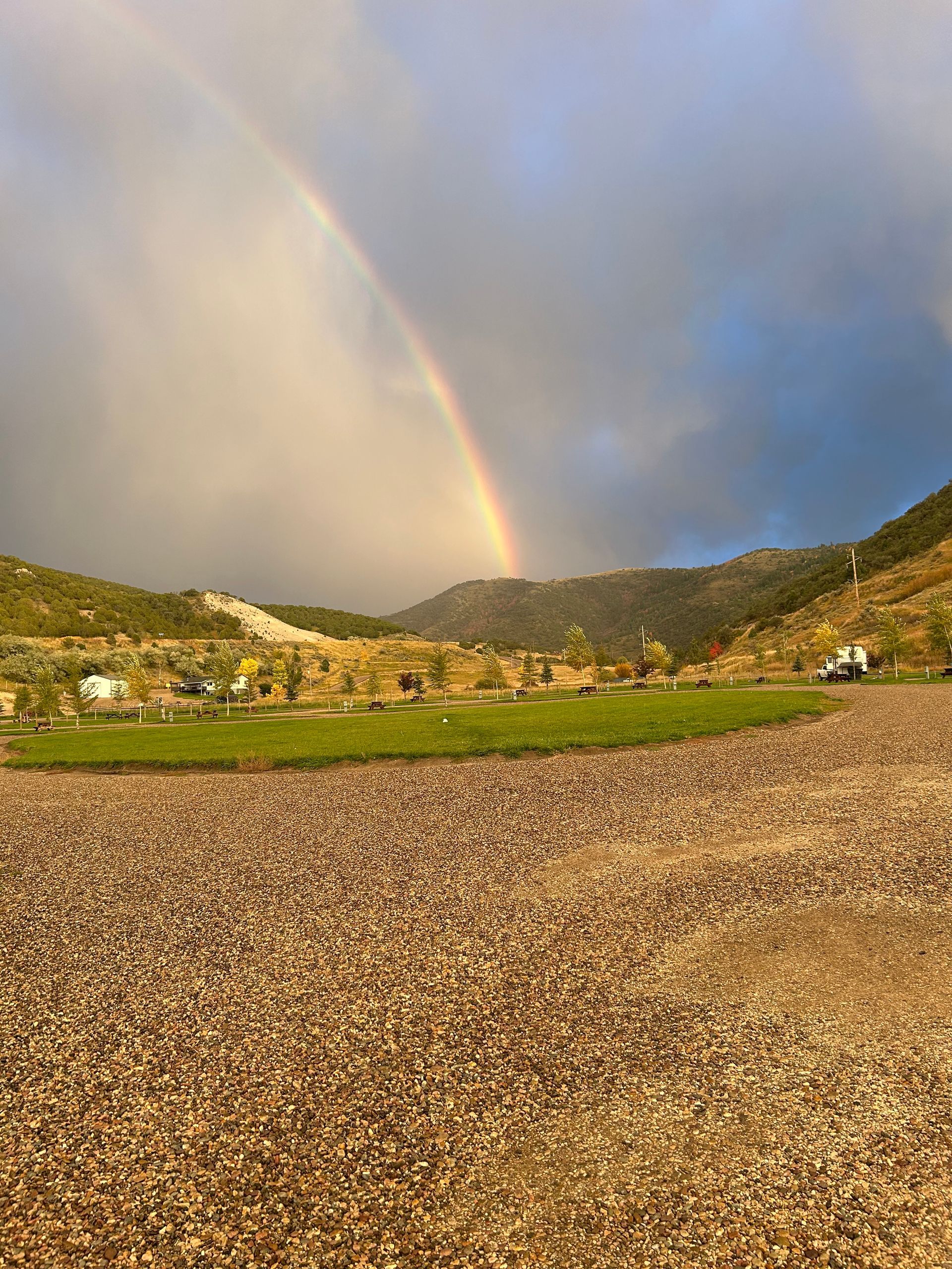 Rainbow over a small hillside village and fields under a cloudy sky