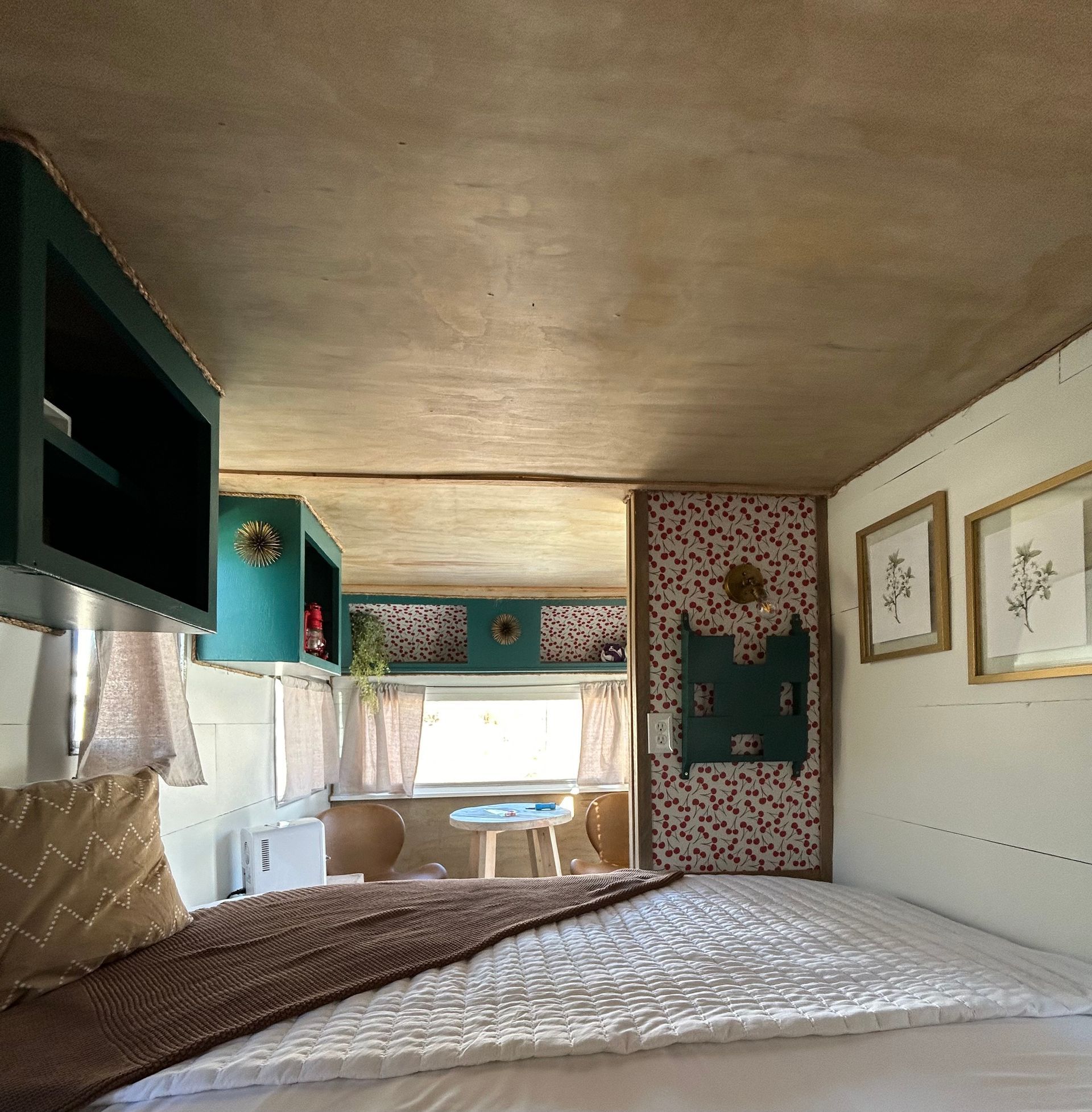 Compact bedroom interior with bed, window seat, teal cabinets, and patterned wallpaper in a small camper-like space