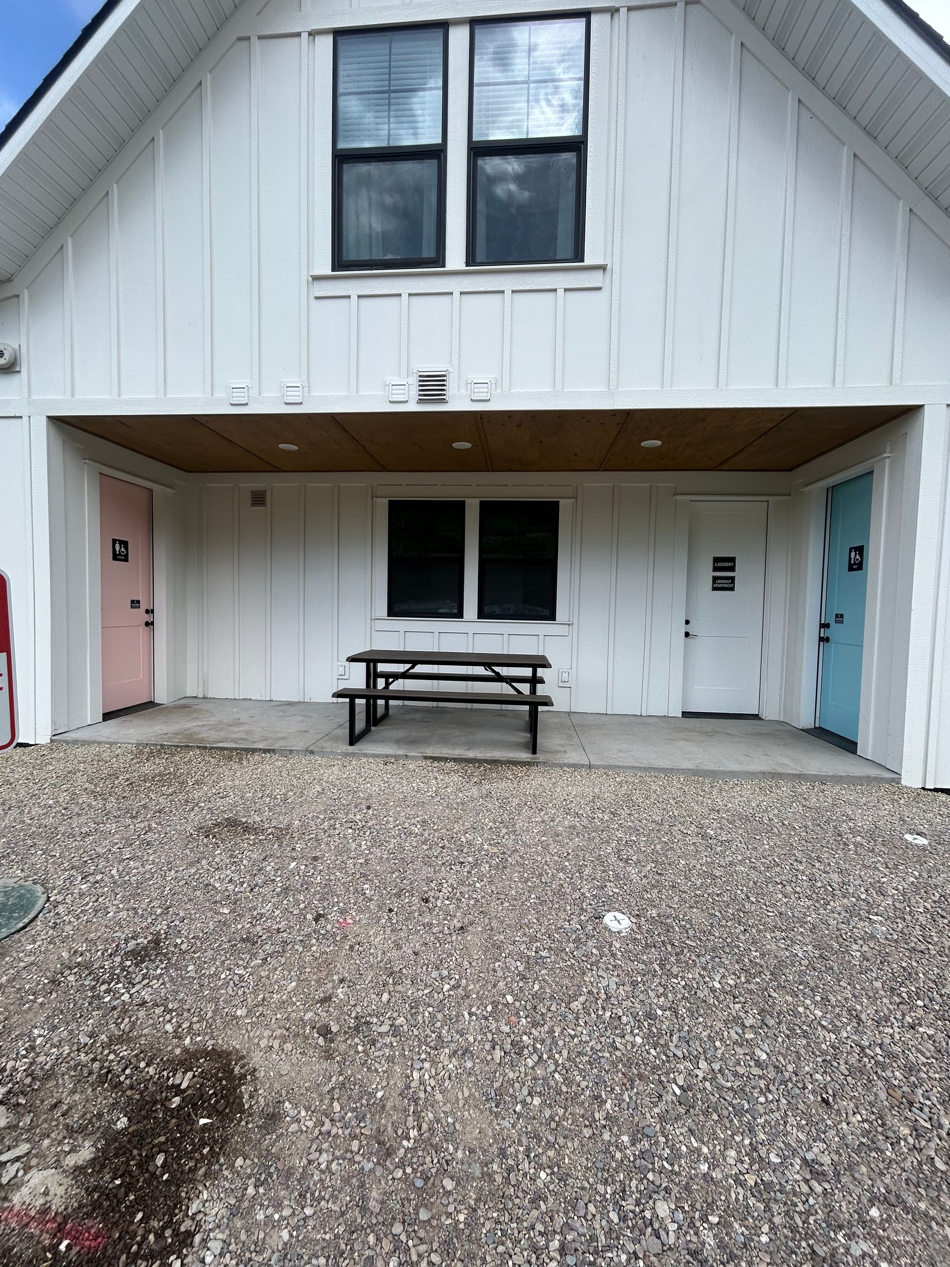 White building entrance with gravel courtyard, picnic table, and two colorful side doors