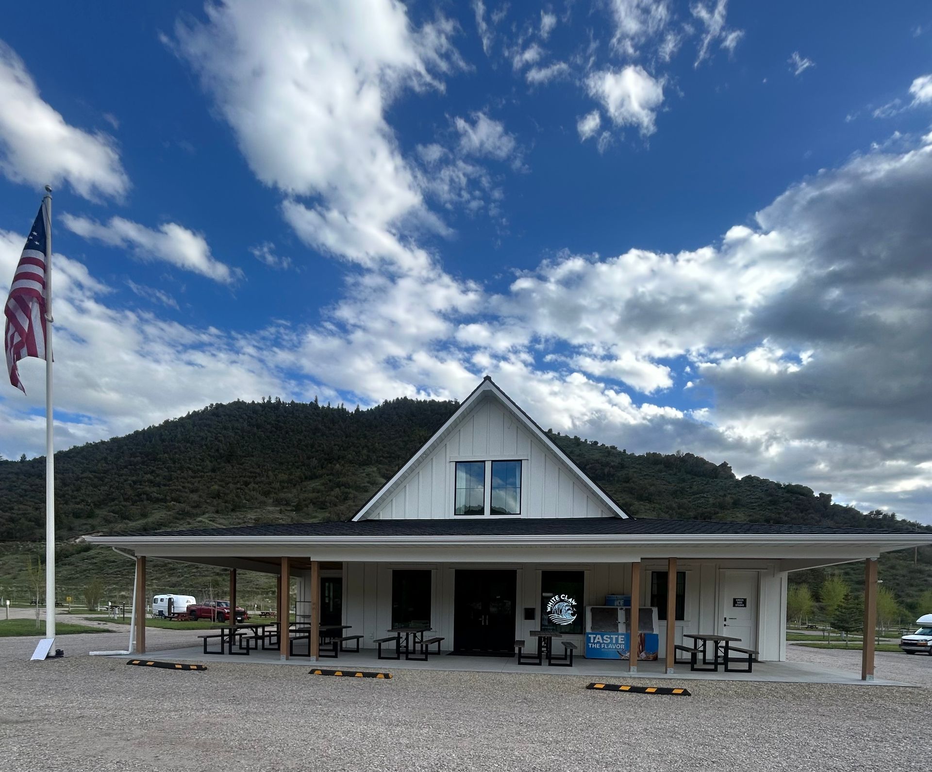 White cabin-style building with a covered porch and American flag under a cloudy mountain sky