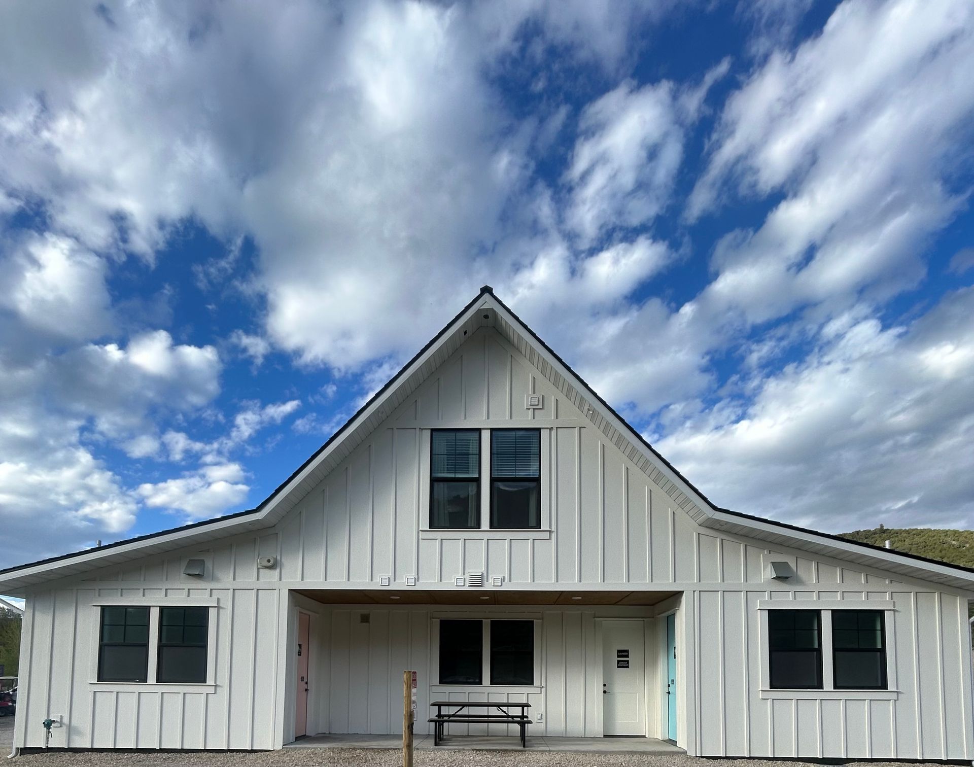 White barn-style building with a steep roof, central entrance, and blue sky with clouds above