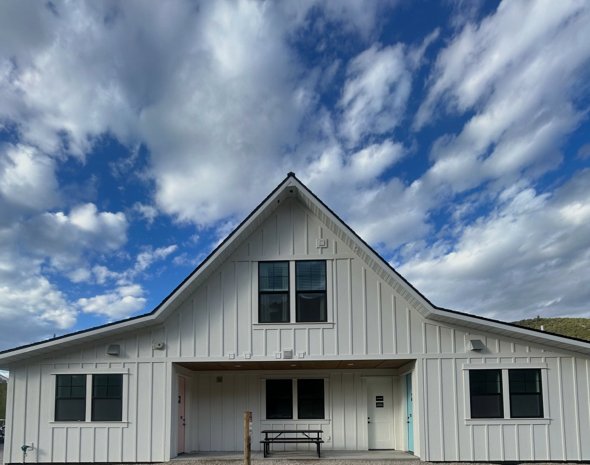 White barn-style house with a peaked roof, black windows, and a cloudy blue sky overhead