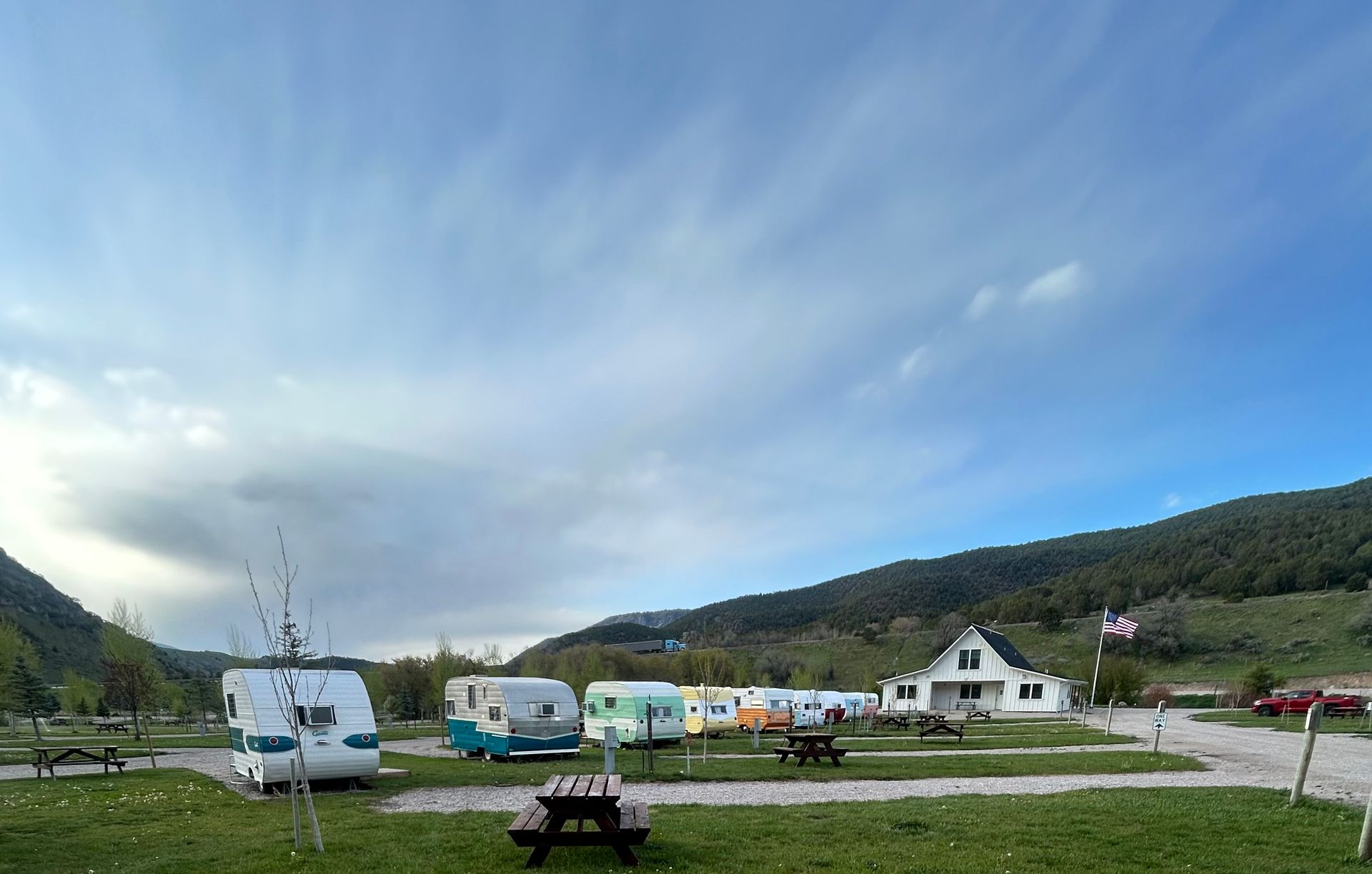 Campground with parked caravans and cabins under a wide blue sky, backed by green hills