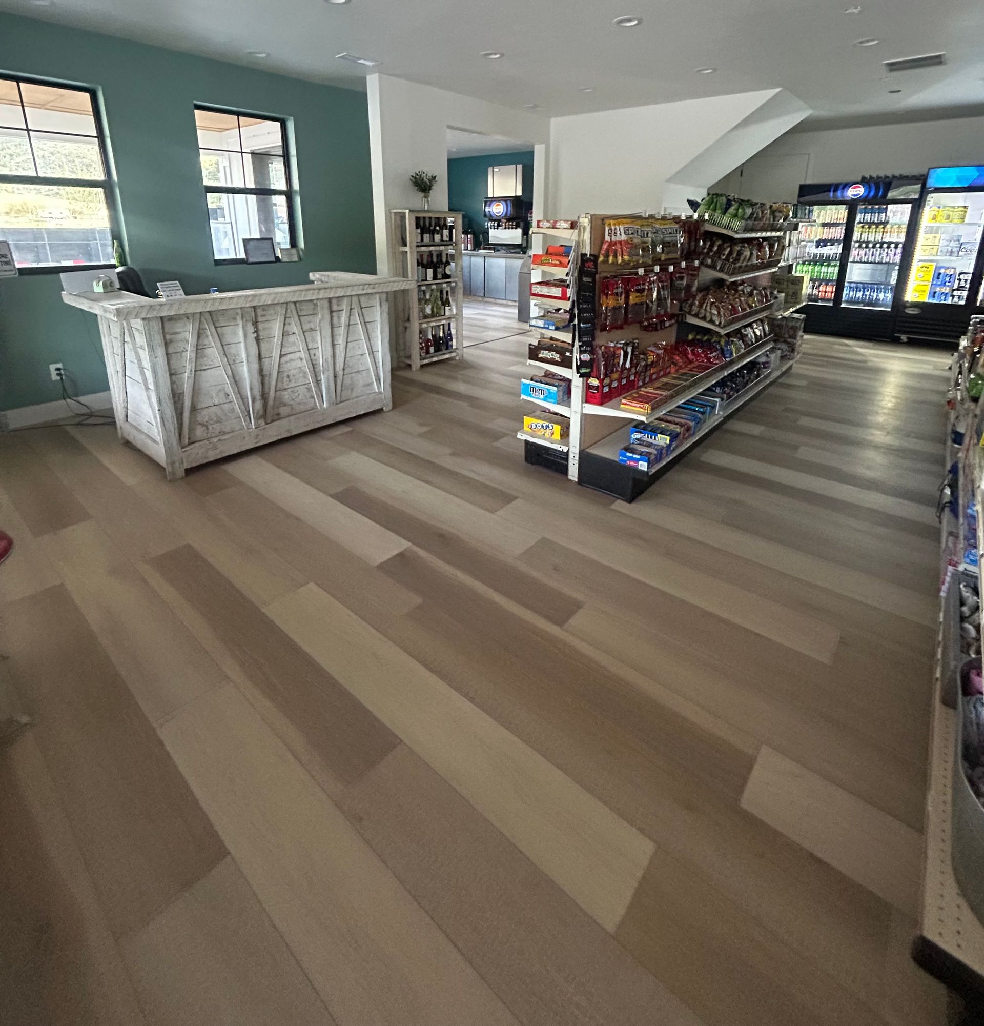 Empty convenience store interior with light wood floors, snack shelves, coolers, and front counter