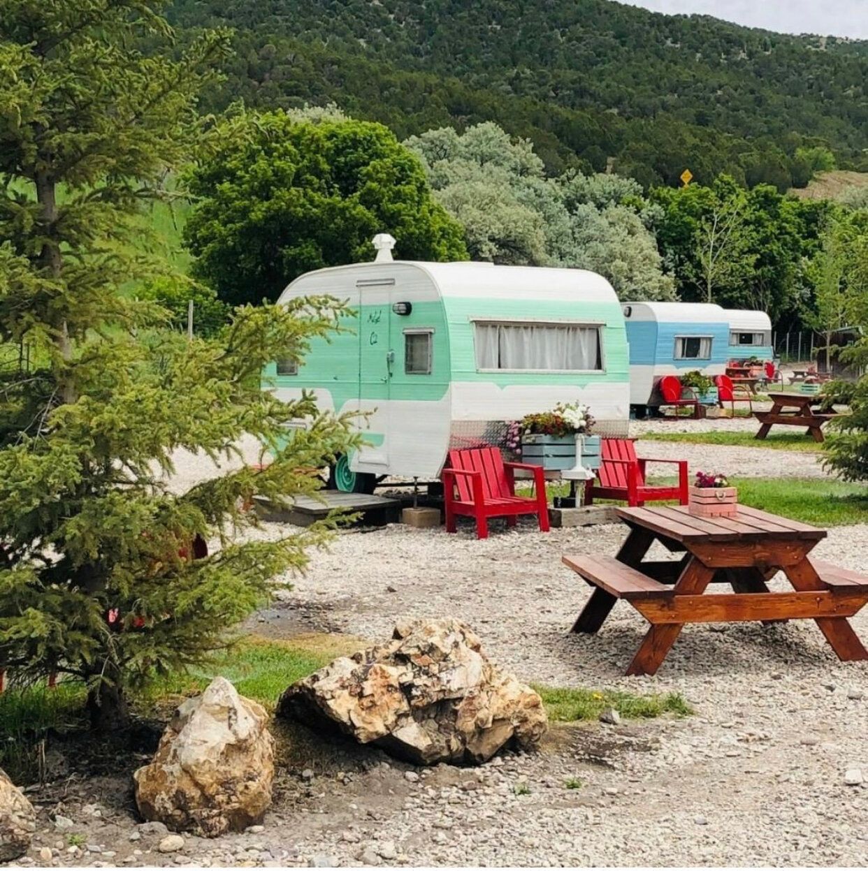 Pastel camper trailers and picnic tables on a gravel campsite surrounded by green hills