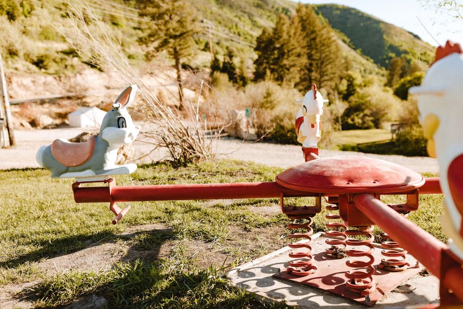 Playground with red seesaw in foreground and people in a sunny mountain park