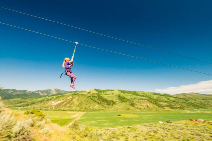 Person ziplining over a green valley under a clear blue sky