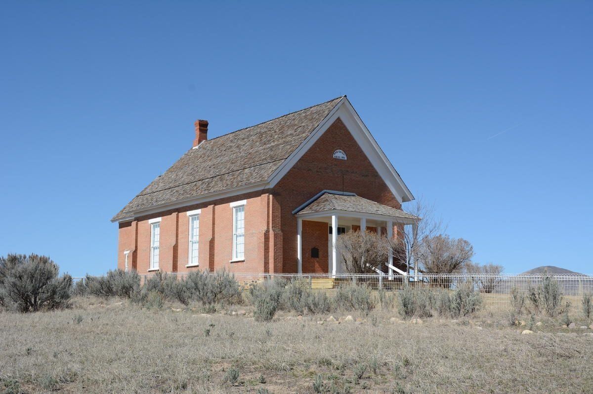 Small red brick house with white trim and a steep roof in a dry field under a blue sky