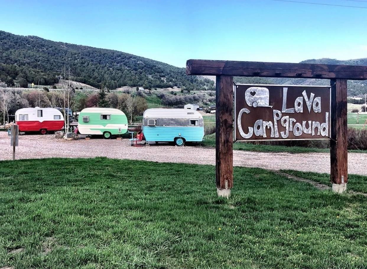 Three colorful trailers beside a sign reading “LaVa Campground” in a grassy mountain campsite.