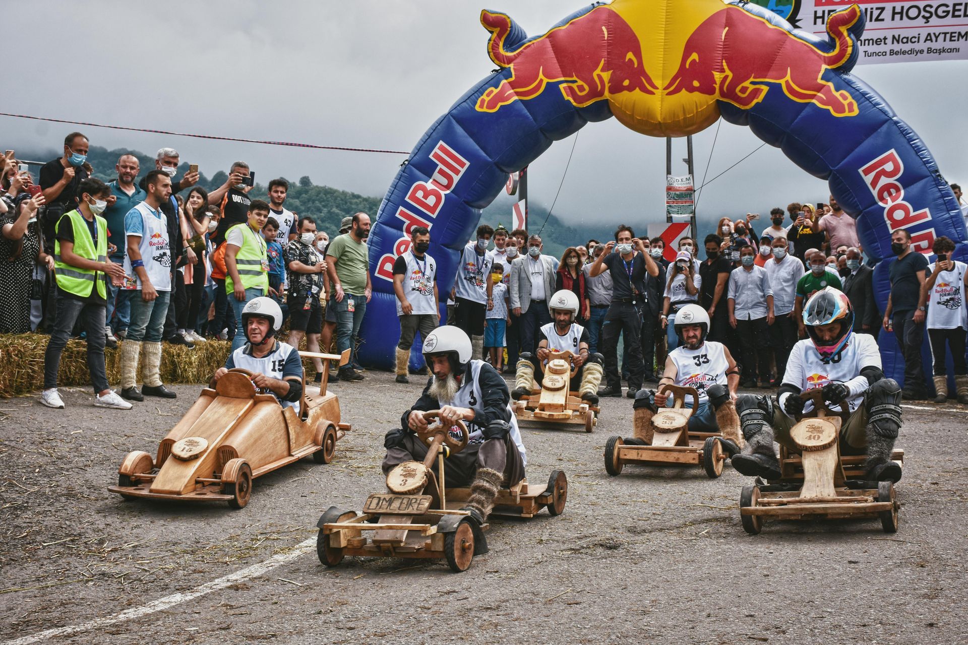 Soapbox race cars lined up at the start under a Red Bull arch, with a crowd watching.