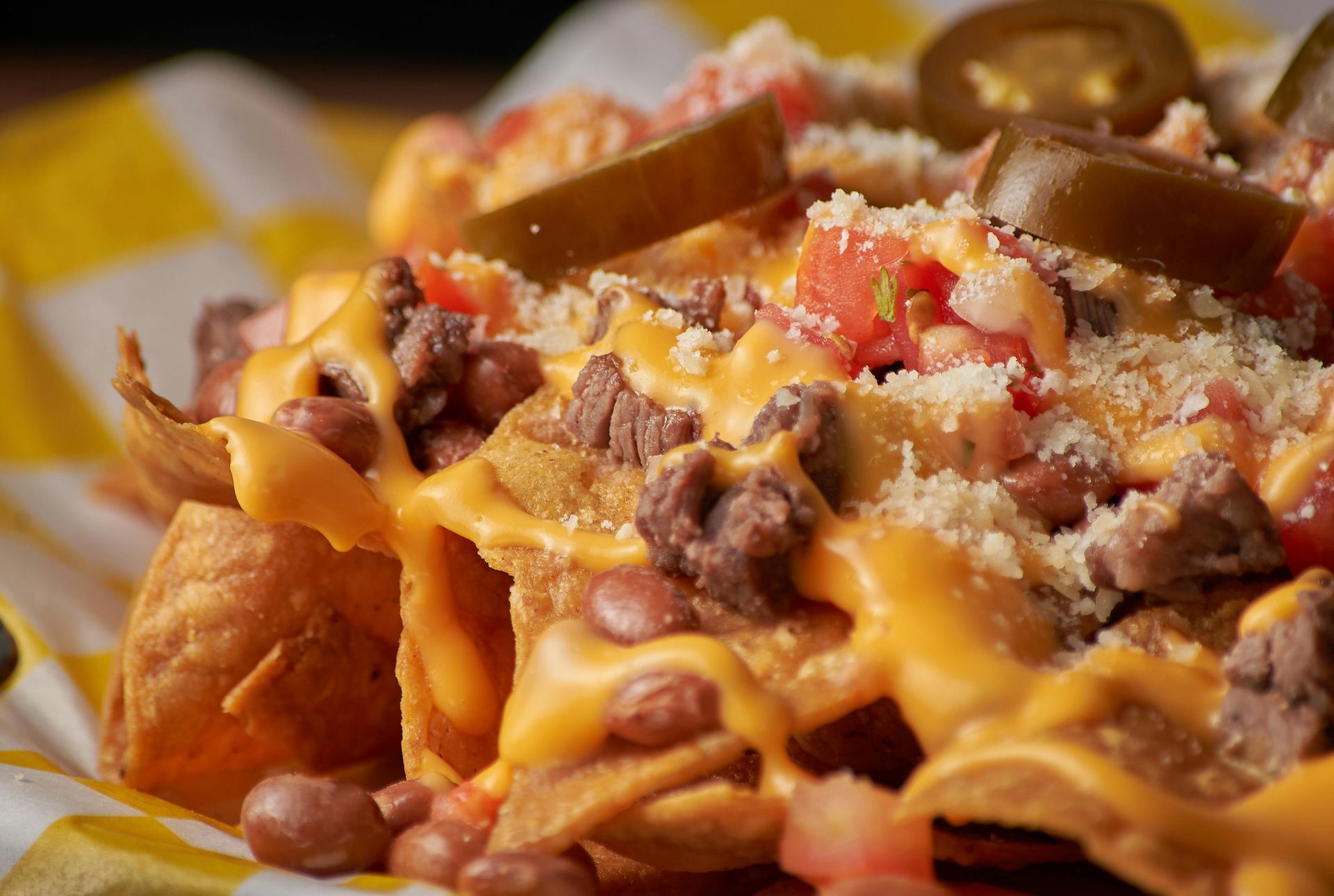 Loaded nachos with melted cheese, beans, tomatoes, and jalapeños on a checkered paper-lined tray