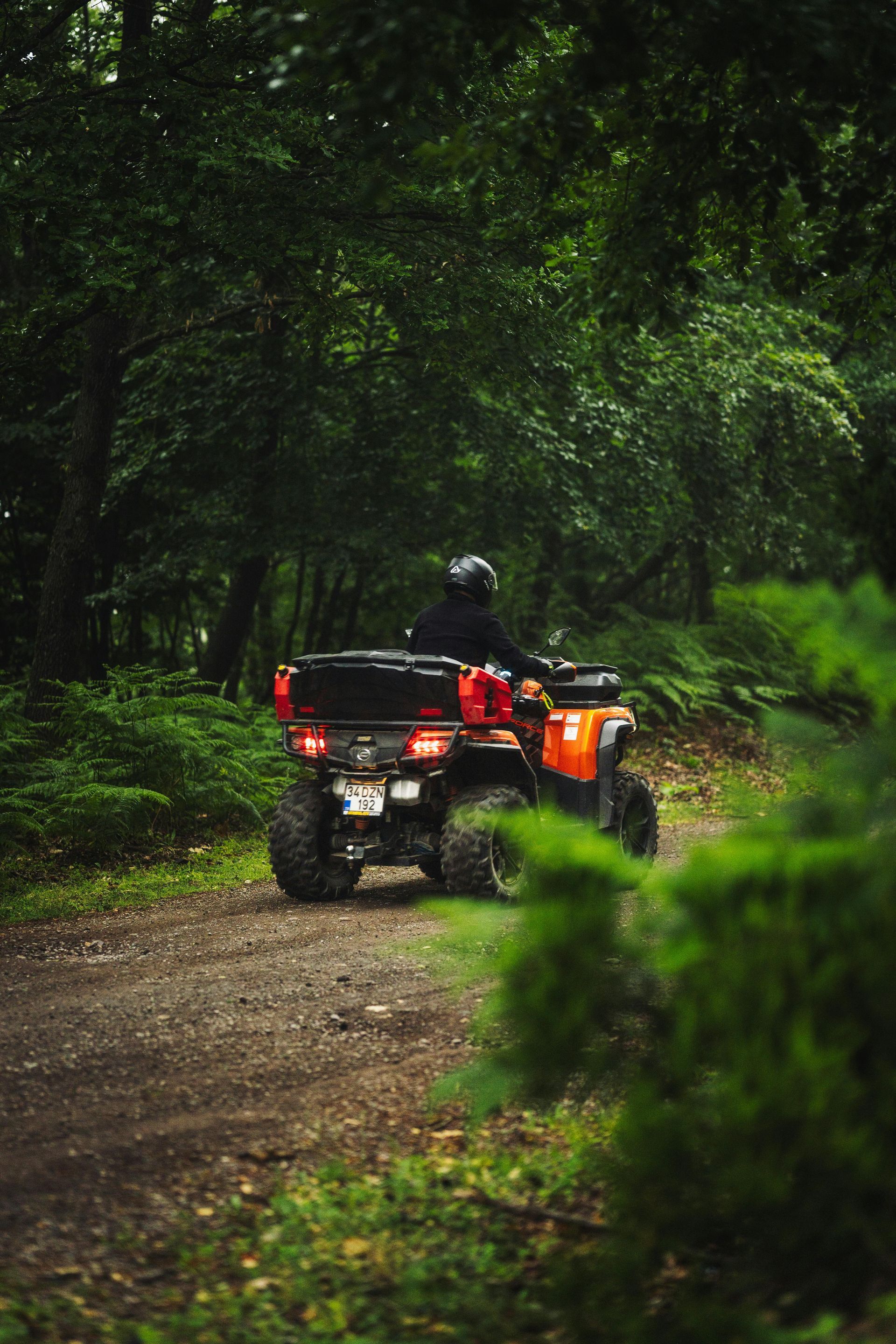 An orange ATV with a rider on a muddy forest trail surrounded by dense green trees.