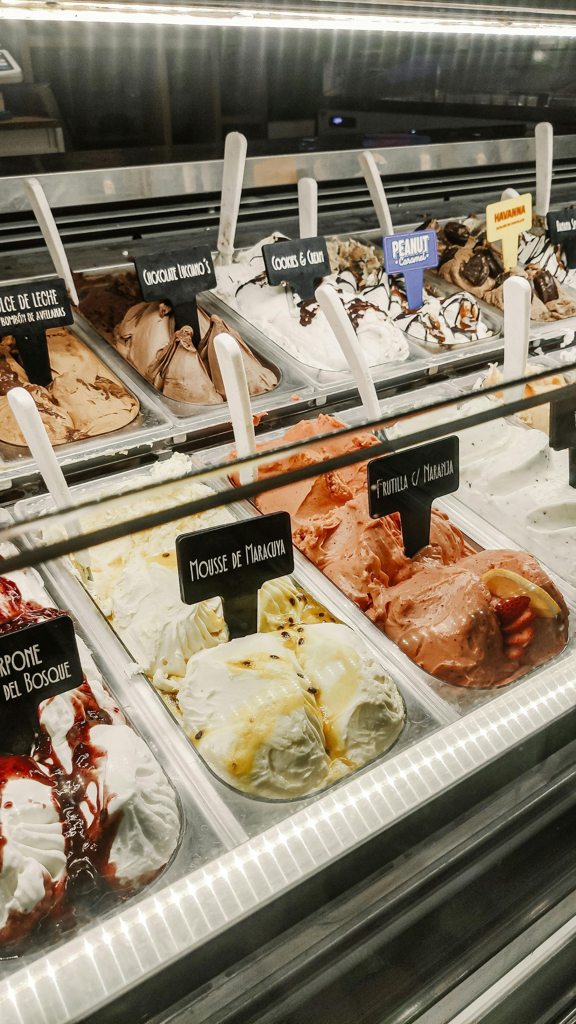 Ice cream display case with assorted flavors in tubs and labels under glass.