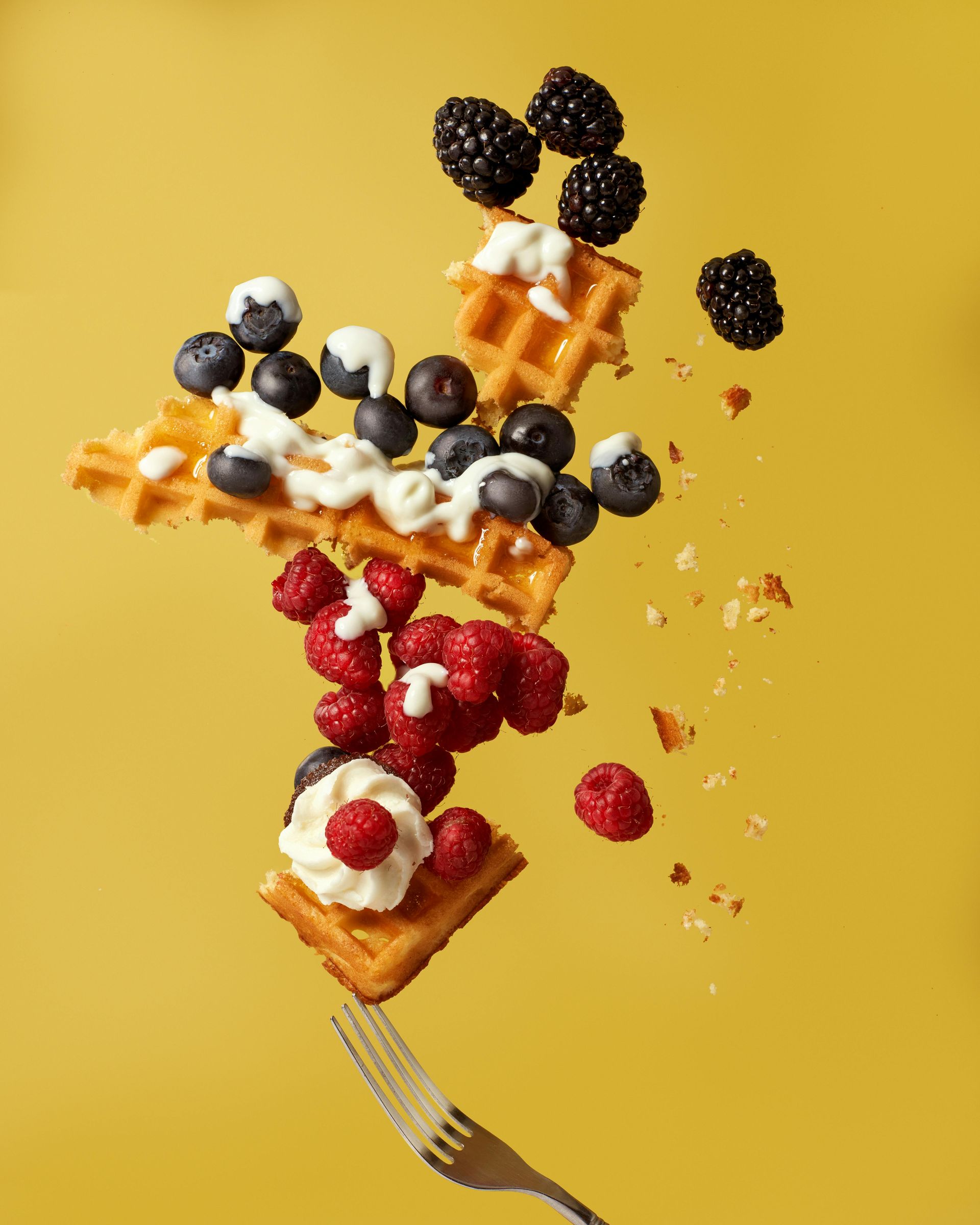 Waffle tower topped with berries and whipped cream on a yellow background, with a fork below