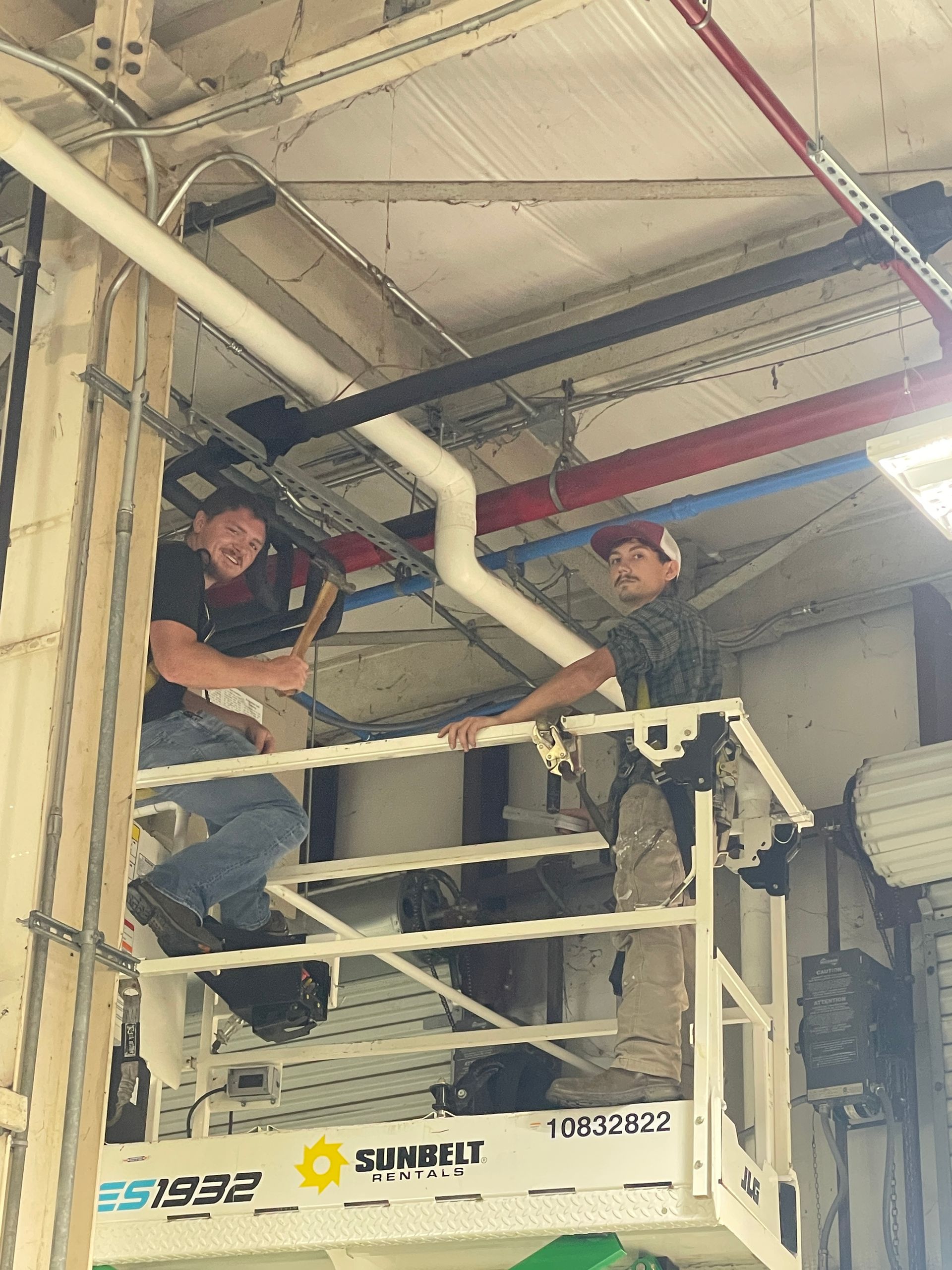 Two men are working on pipes in a building.