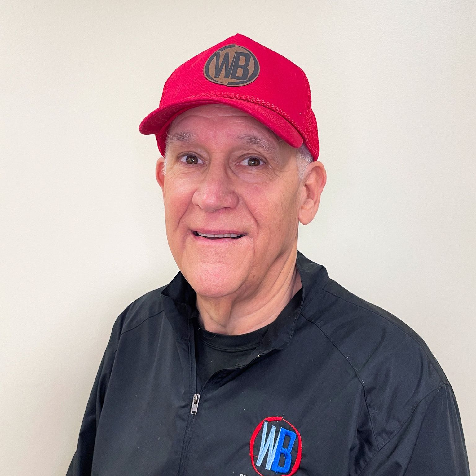 A man wearing a red hat and a black jacket is smiling for the camera.