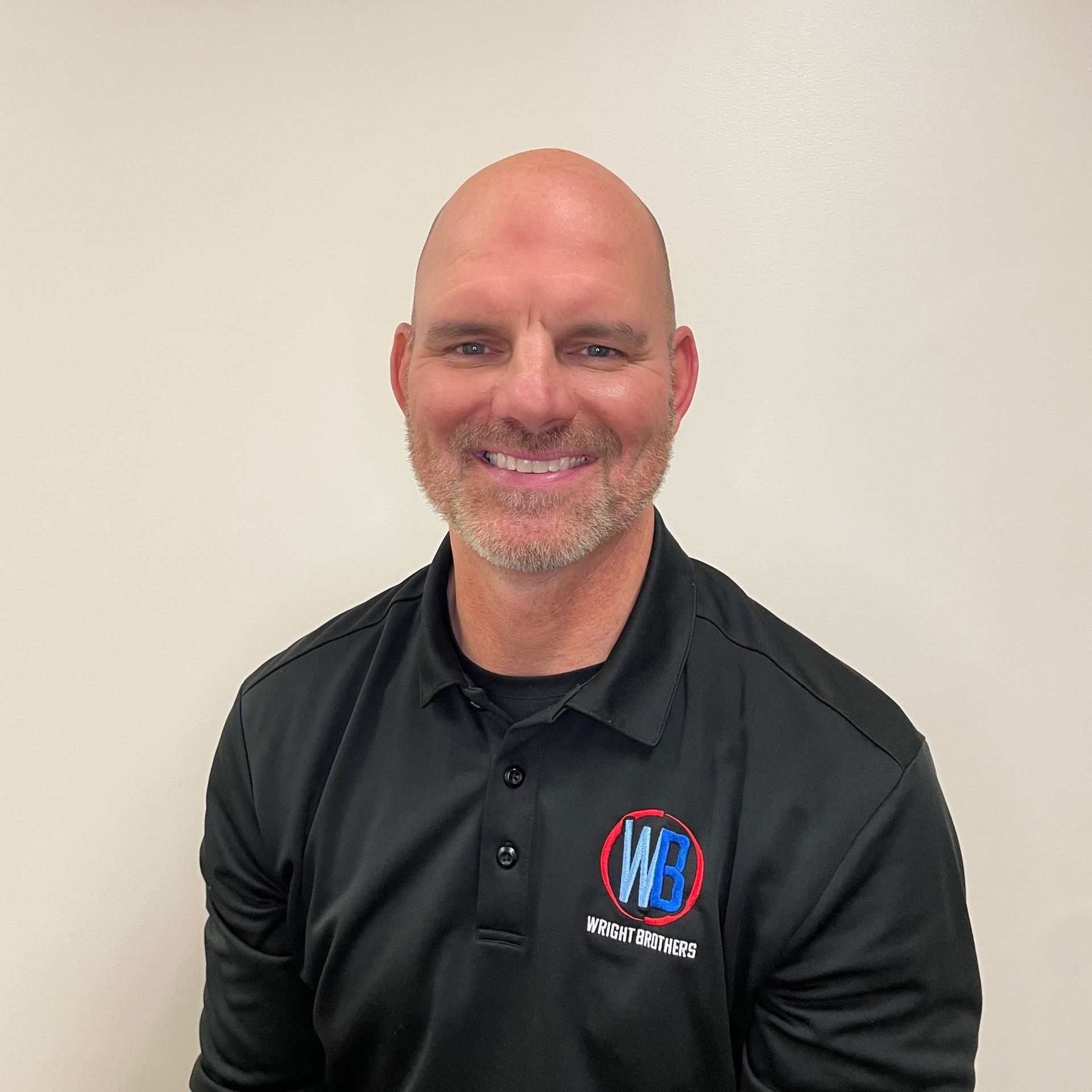 A bald man with a beard is wearing a black polo shirt and smiling.