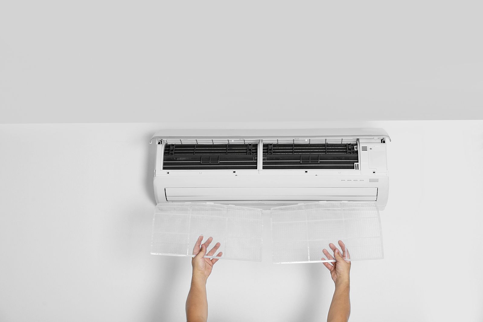 A person is cleaning an air conditioner on a white wall.