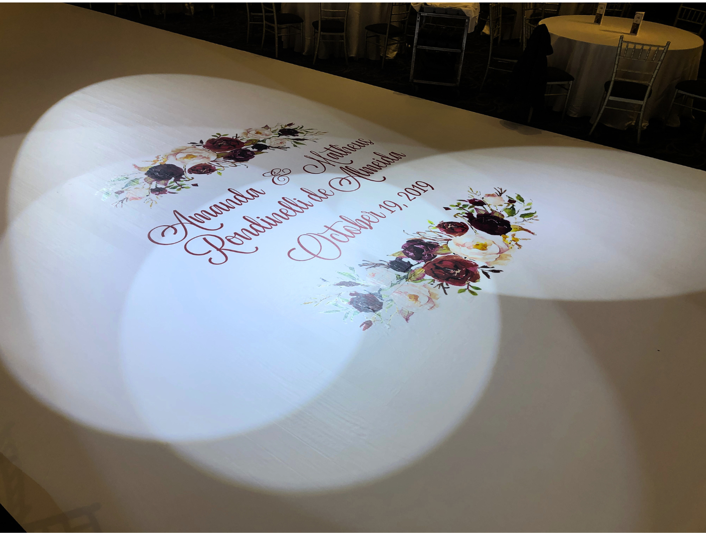 A wedding invitation is projected on a dance floor