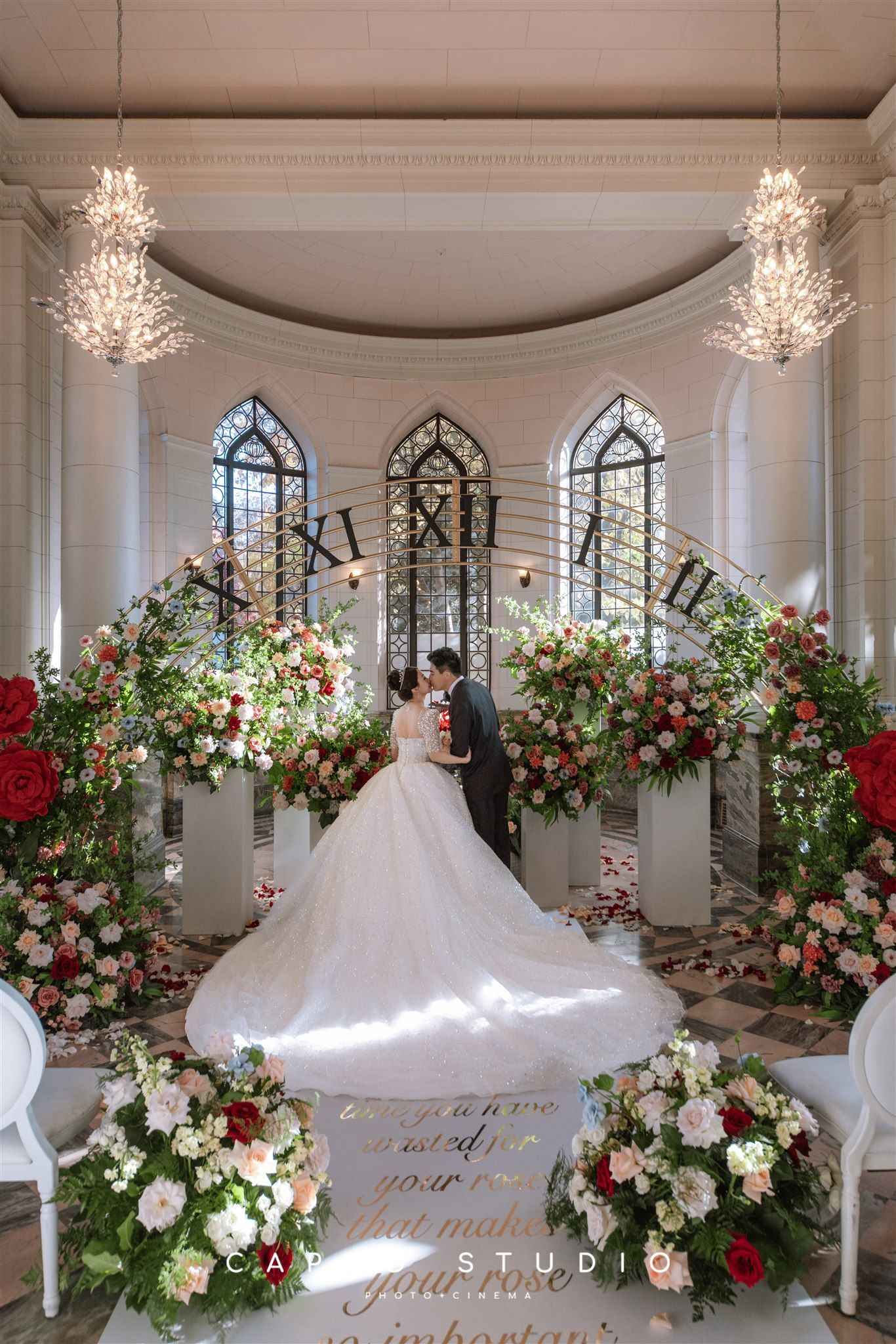 A bride and groom are kissing in a church surrounded by flowers.
