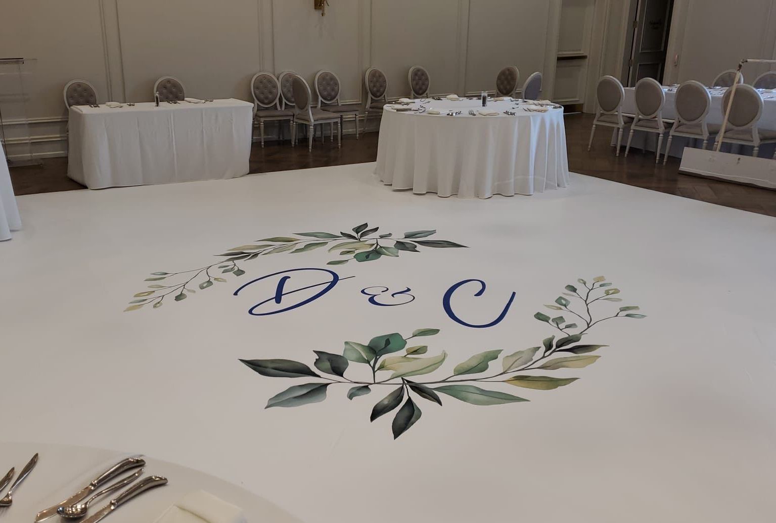 A large room with tables and chairs and a dance floor with a monogram on it.