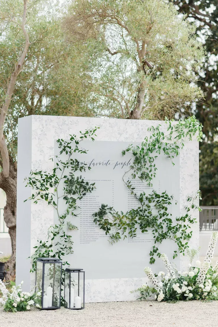 A white wall with greenery growing on it and lanterns in front of it.