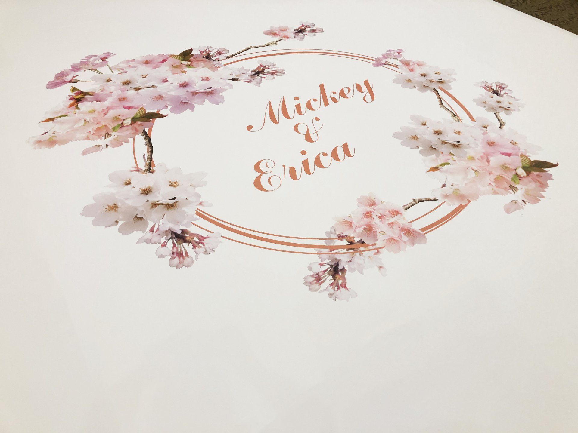 A wedding invitation with a wreath of flowers and the names mickey and erica