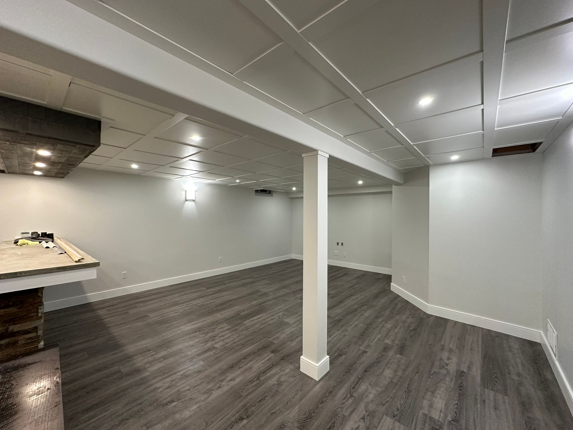 An empty basement with hardwood floors and white walls.