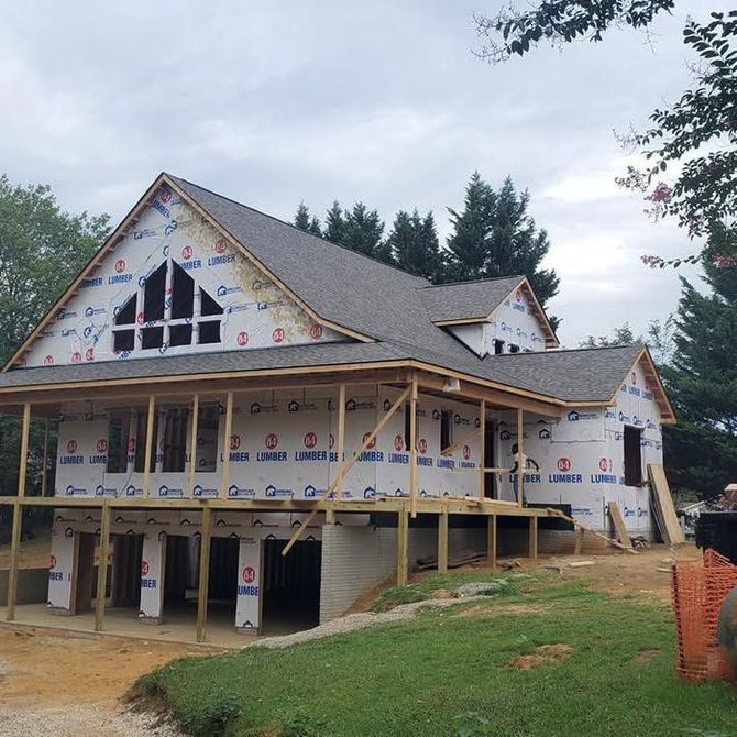 Partially built house with gray roof, white siding, and exposed framing on a grassy lot