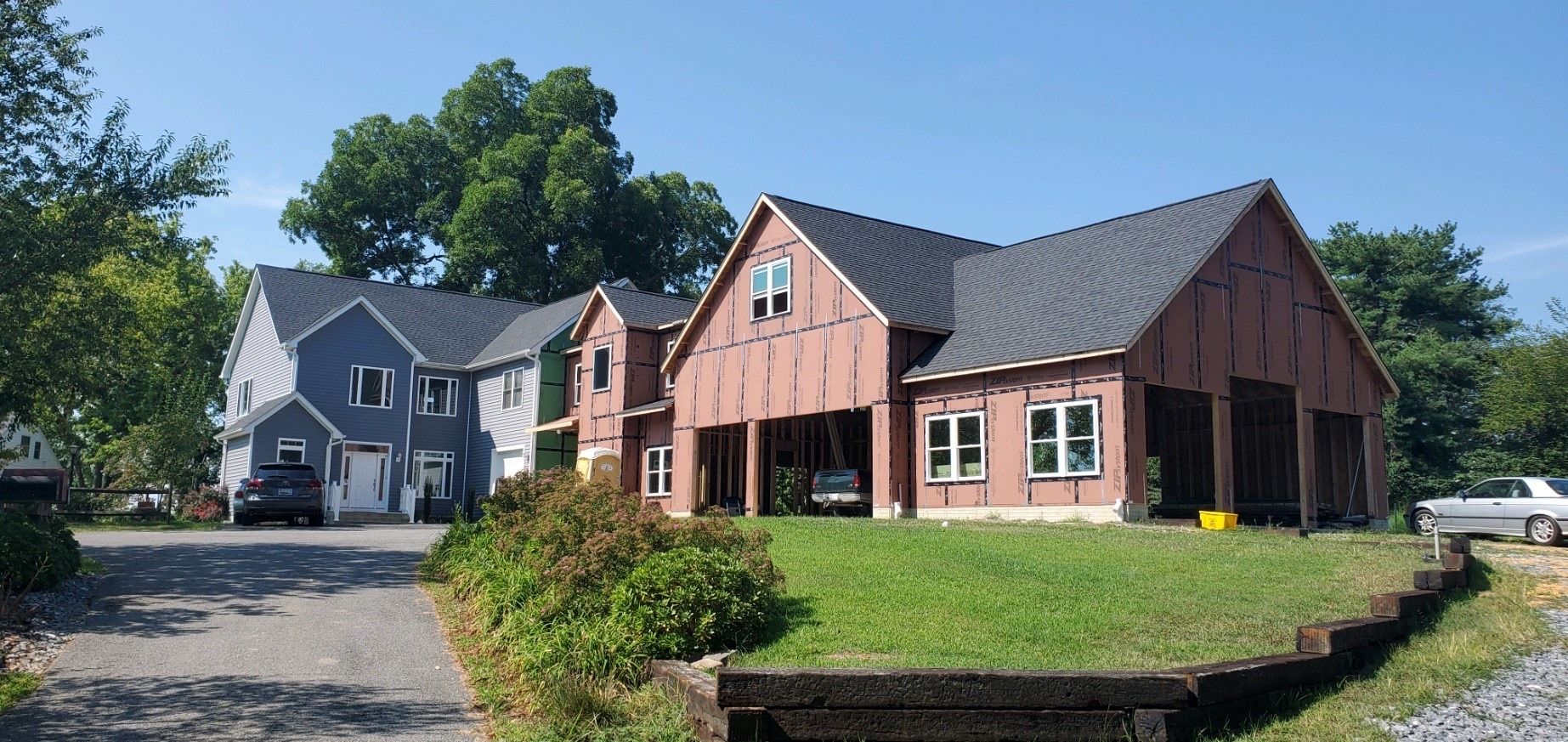 A red brick building and a gray house beside a gravel drive, with trees and a grassy lawn in front.