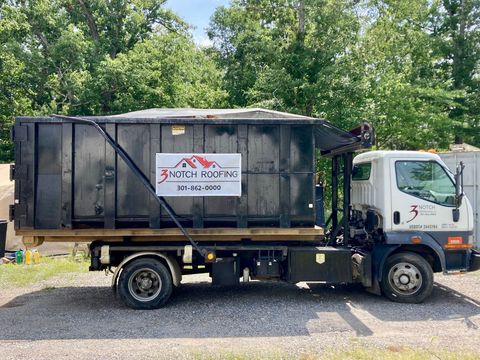 Three Notch Roofing dump truck parked on a street, with company logo on the door and utility compartments on the side